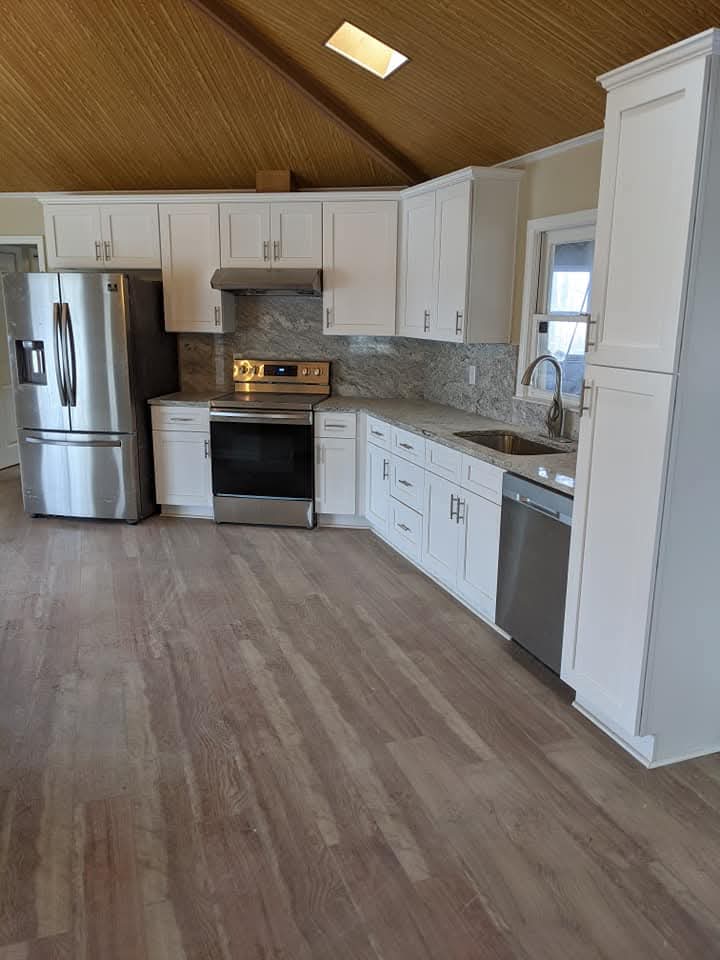 A renovated kitchen with white shaker-style cabinets, stainless steel appliances, granite countertops with a matching full-height backsplash, and light wood-plank flooring.
